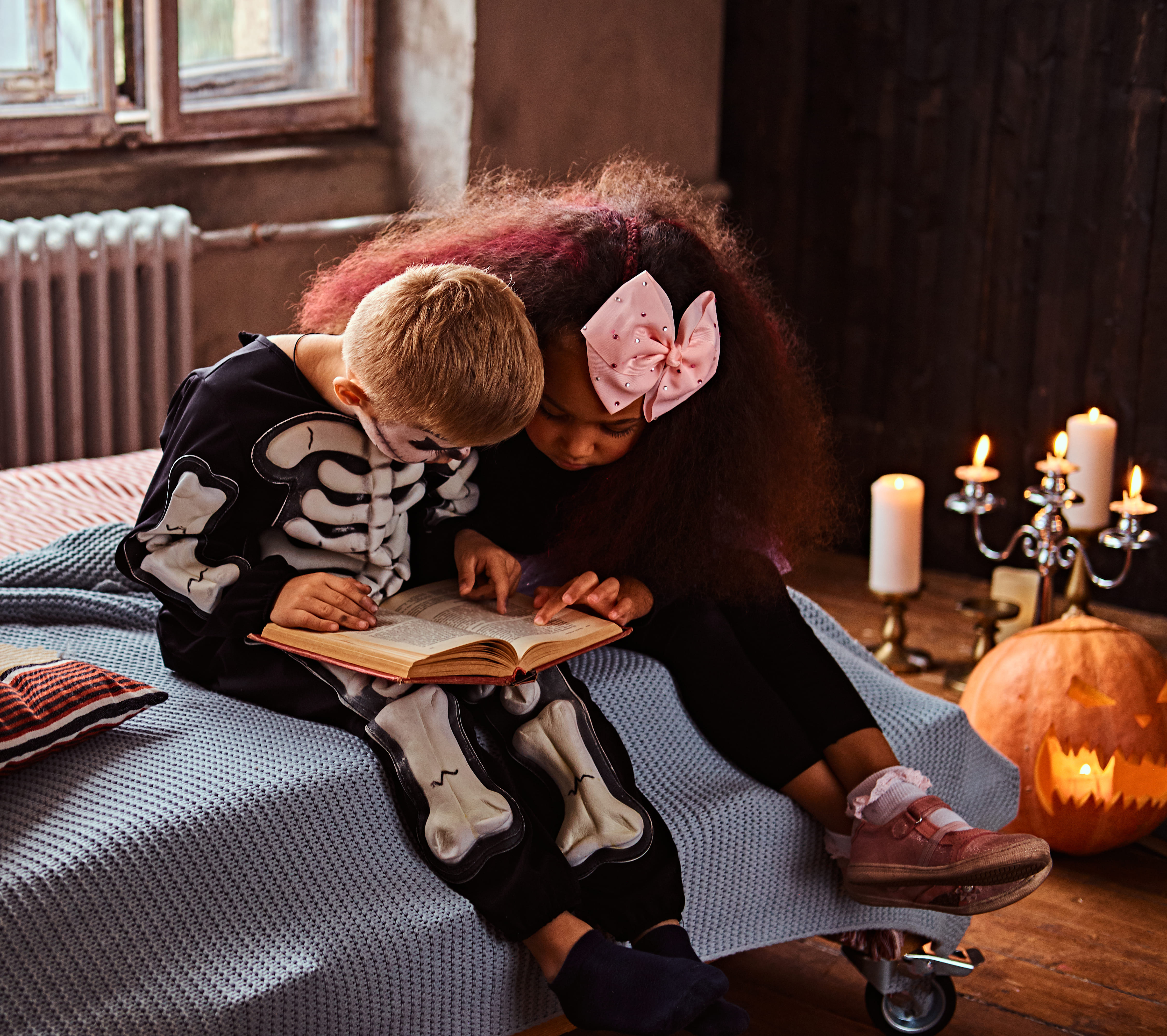 three multiracial kids scary costumes reading horror stories while sitting bed old house halloween concept 1